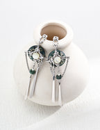 White-gold sterling silver drop earrings with circular green moss agate, pale mother-of-pearl centers, suspended chains and elongated metal bars.