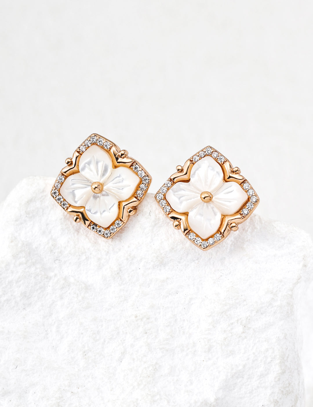 White-gold sterling silver stud earrings with four white mother-of-pearl petals, cubic zirconia accents and a softly squared frame.