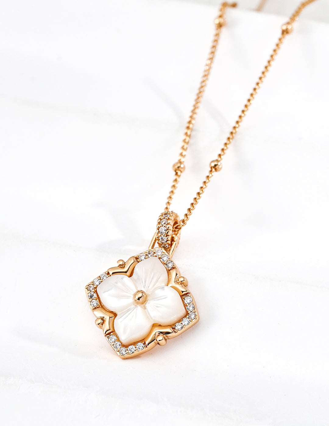 Vintage-gold sterling silver necklace with carved four-petal mother-of-pearl pendant, cubic zirconia accents and a softly squared open frame.